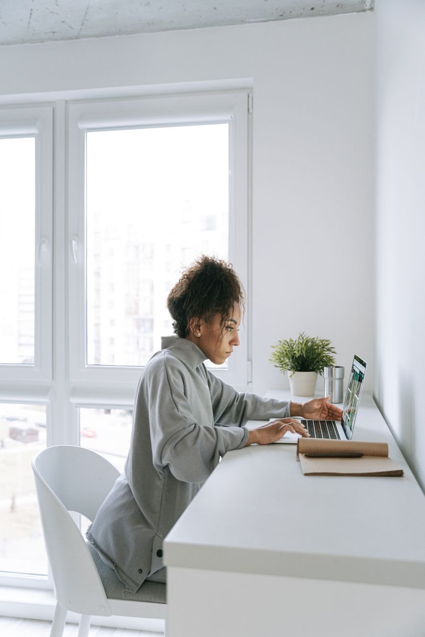 A woman working on her laptop at a home office desk in a modern, bright room.